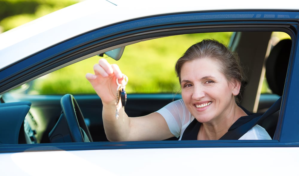 Close up of a smiling  woman, buyer sitting in her new white car holding up car keys