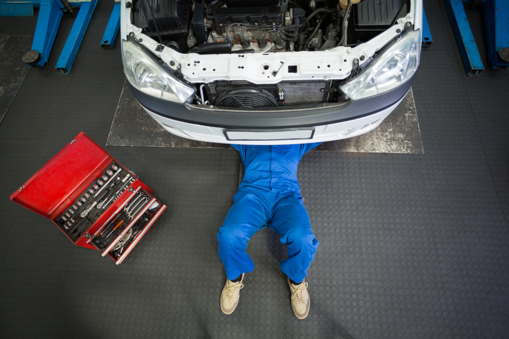 Technician laying under the front end of a car with the hood raised